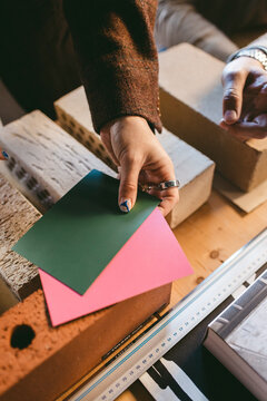 High angle view of female designer's hand holding papers on bricks while showing design process in office