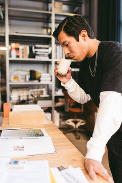 Focused male architect drinking coffee while reading magazine for design process in office