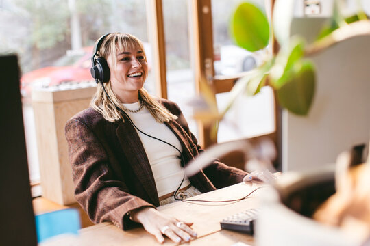 Happy young female design professional wearing headphones working in office