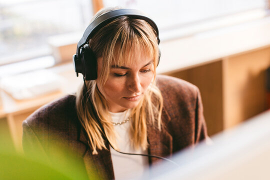 Concentrated young business expert working with wired headphones in office