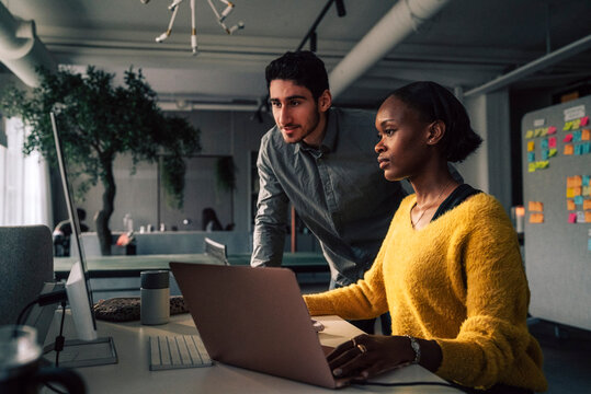 Young male programmer standing beside female colleague using desktop PC in office