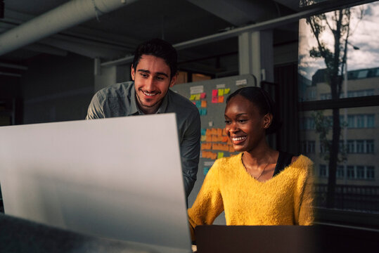 Smiling female programmer using computer while sitting beside male colleague in tech office
