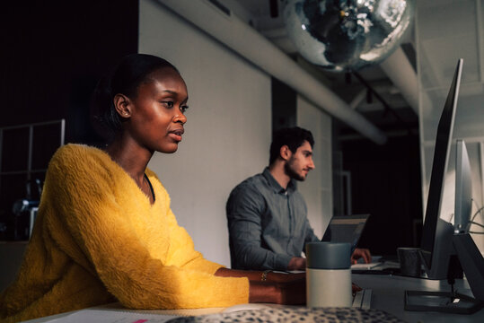 Focused female tech expert working on desktop PC while sitting with male colleague in startup office