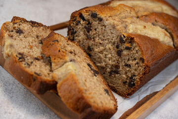Freshly baked banana bread is sliced and displayed on a wooden cutting board. The bread has a golden-brown crust and chocolate chips, perfect for a cozy snack at home.