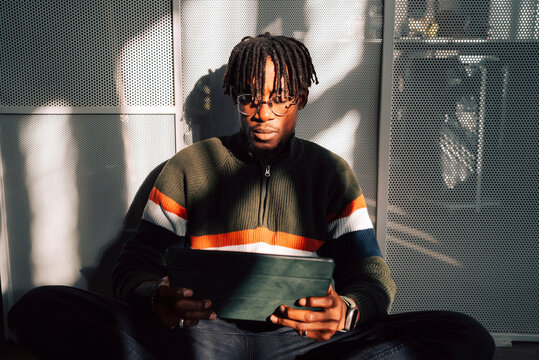 Male business professional with braided hair using tablet PC while sitting in office