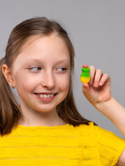 smiling girl in a close-up shot against a light neutral background. She has fair skin and light brown hair styled in two low pigtails. She is wearing a bright yellow knitted T-shirt that matches well 