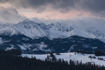 Scenic winter landscape of the Tatra Mountains at dawn. Snow-covered peaks and frosty pine forests under a crisp blue morning sky.