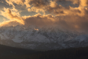 Scenic winter landscape of the Tatra Mountains at dawn. Snow-covered peaks and frosty pine forests under a crisp blue morning sky.