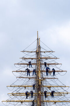 Ship mast rigging and sailor maritime training captures teamwork at height with strict safety discipline beneath wide blue sky on tall vessel