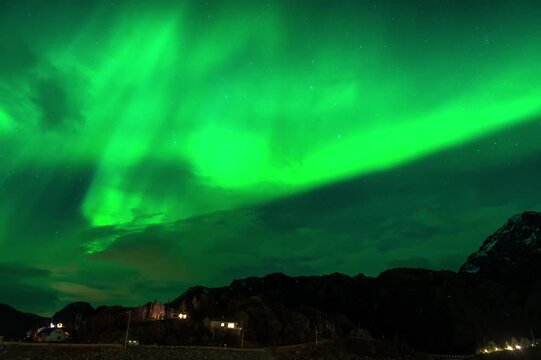 Massive Northern lights (aurora borealis) KP3 appearing green over the sky at a dock with boats in Senja island, Norway
