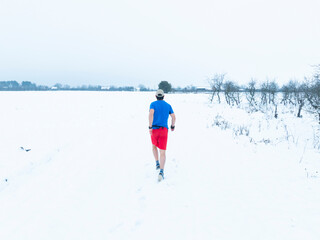 A man jogging on a snow path alone thus improving his health