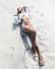 Black and white photograph of a black woman lying on white sand at the beach. Minimalist coastal scene highlighting contrast, calmness, relaxation, summer mood, and timeless elegance. Artistic monochr