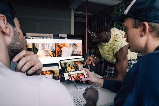Male creative tech expert discussing with colleagues while checking responsive design preview on different devices in of