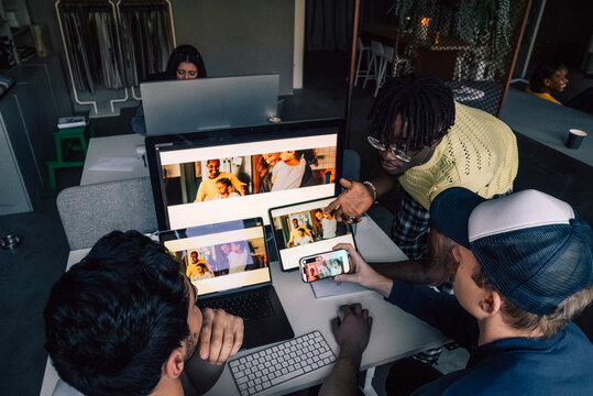 High angle view of male creative tech expert discussing with colleagues while checking responsive design preview on diff