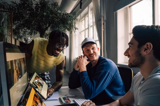 Smiling male creative tech professionals working on responsive design preview on with devices in office