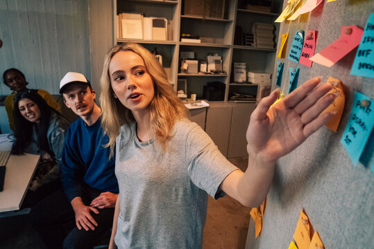 High angle view of young businesswoman explaining pointers through adhesive note to team in startup office