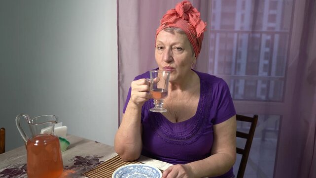 Elderly woman drinks compote from a glass at home