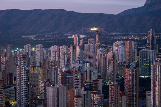 Aerial twilight skyline city night lights over urban buildings with mountains in benidorm spain creating a dramatic evening panorama