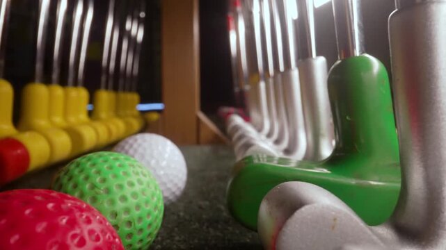 Colorful mini golf balls and putters lined up on a rack. Leisure and entertainment concept showing sports equipment for a fun family game