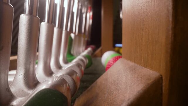 Close-up of mini golf putters of various sizes and colors organized in a wooden rack, with colorful golf balls ready for the game