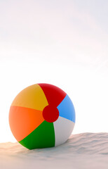 Fototapeta premium Vibrant colourful beach ball on a sandy beach in bright sunshine in summer showing family vacation 3d render