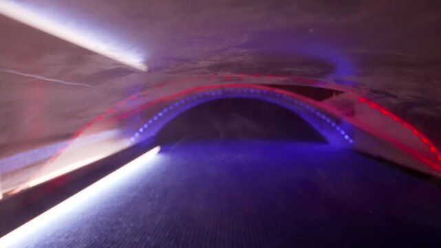 Slow motion of an orange table tennis ball bouncing on a futuristic surface. The scene is illuminated by glowing blue and red neon lights