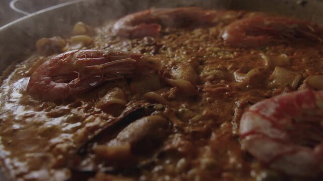 Macro view of traditional seafood paella cooking slowly with bubbling rice steam and subtle movement in the pan