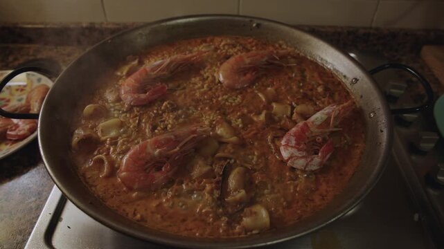 Traditional Valencian seafood paella cooking slowly in a pan with prawns squid mussels steam and boiling bubbles
