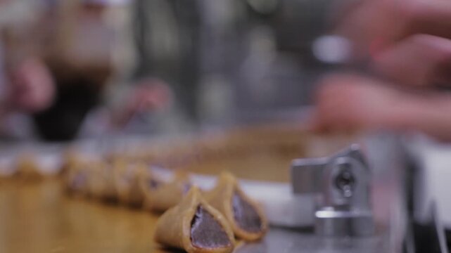 close-up of employee filling triangular pralines with chocolate before conveyor placement.