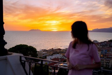 Fototapeta premium Woman watching sunset over sea from balcony