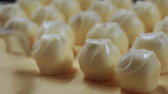 Close-up of neatly arranged glossy white chocolate-coated round pralines on factory tray.