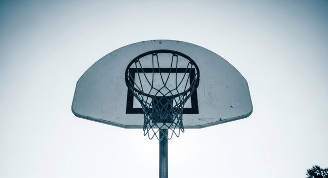 Basketball hoop silhouette against a pale sky, upward view, minimal color