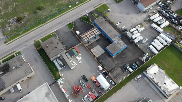 High angle drone footage flying over a commercial district. Industrial buildings, warehouses, parking lots with cars, rvs and boats are visible. In ajax ontario canada