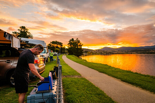 a man cooking on a improvised kitchen on a camping ground next to a lake during sunset
