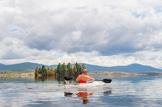 man kayakinng on a glassy lake during the day