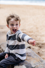 Happy young boy playing on the beach, pointing excitedly at something interesting