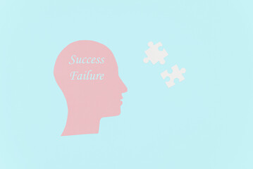 A conceptual illustration of a human head silhouette with the words 'Success' and 'Failure' inside. White puzzle pieces float nearby against a light blue background.