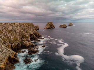 Obraz premium Long-exposure aerial view of Pen Hir cliffs and rocky islands, capturing smooth ocean waves, rugged coastline, and dramatic seascapes along the Brittany coast.