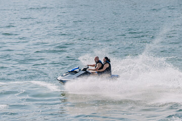 Two individuals riding a jet ski on a sunny day, splashes of water visible as they navigate across the surface of the ocean