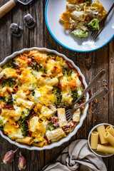 Naklejka premium Pasta casserole with broccoli and smoked bacon on wooden table. Top view