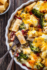 Naklejka premium Pasta casserole with broccoli and smoked bacon on wooden table. Top view