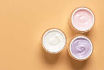 Set of colored cosmetic creams in open jars on pastel yellow background , top view, flat lay,