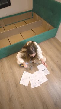 Young Woman Constructing Bed Frame Carefully. Caucasian Woman Struggles With Bed Assembly At Home