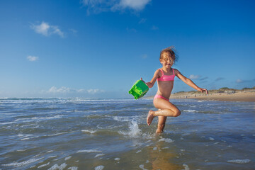 Child girl joyfully playing in ocean waves with green bucket