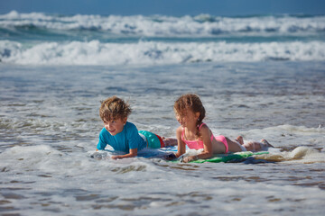 Kids playing lay on surfboards in ocean waves at beach vacation