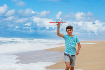 Teenage boy playing with toy airplane on beach during summer