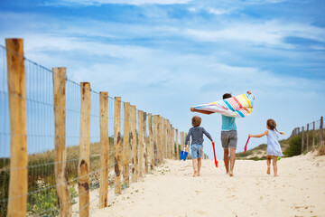 Children hurrying up on sandy path to beach with colorful toys