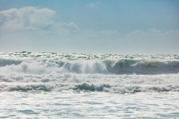 Powerful ocean foamy waves falling and crashing on a sunny shore