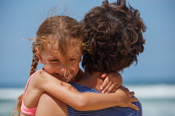 Child girl hugging her parent on beach with waves and blue sky