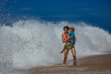 Mother and child boy playing in foamy ocean waves on sunny beach